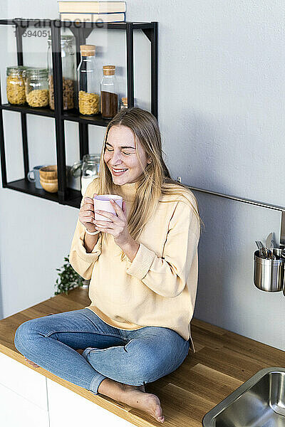 Smiling woman with coffee cup day dreaming in kitchen