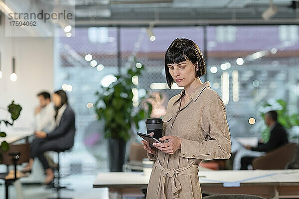 Manager mit Einwegkaffeetasse und Smartphone im Büro