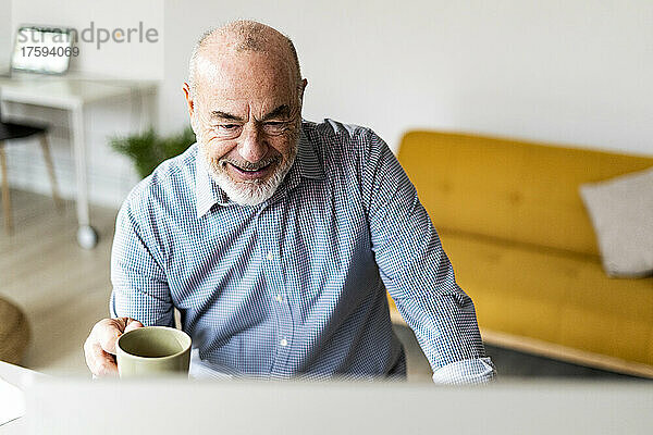 Smiling senior businessman holding coffee mug at home