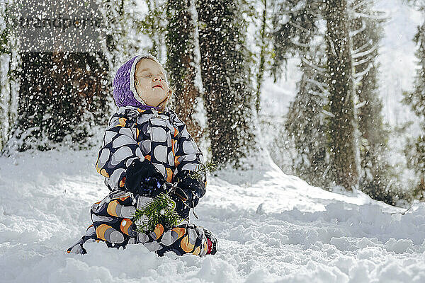 Girl with eyes closed enjoying snowfall in winter forest
