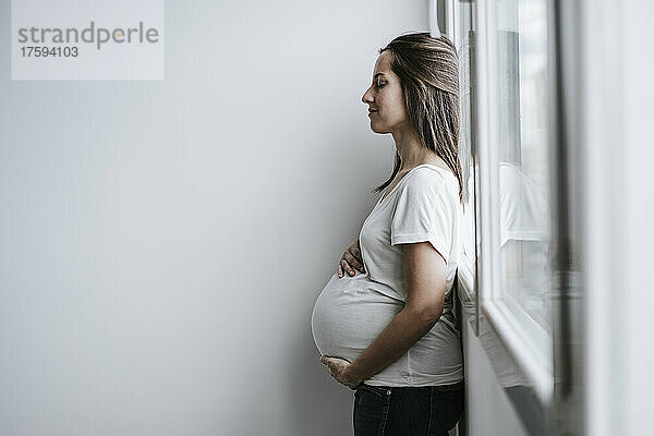 Schwangere Frau lehnt zu Hause am Fenster