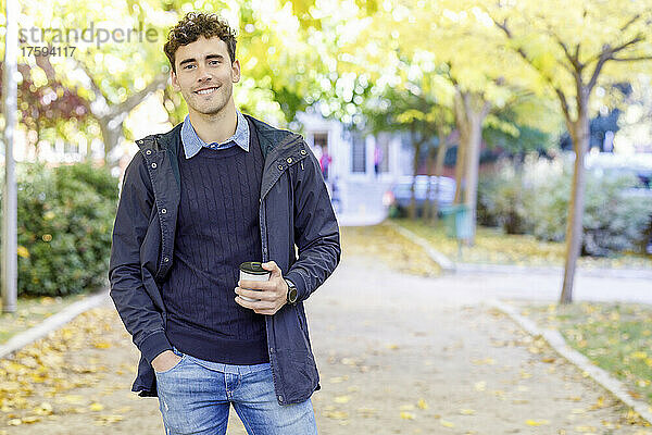 Lächelnder Mann mit Einweg-Kaffeetasse im College-Park