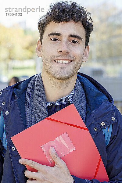 Lächelnder Mann mit roter Akte auf dem Campus