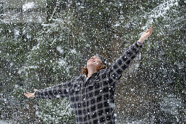 Glücklicher junger Mann in warmer Kleidung  der den Schneefall genießt