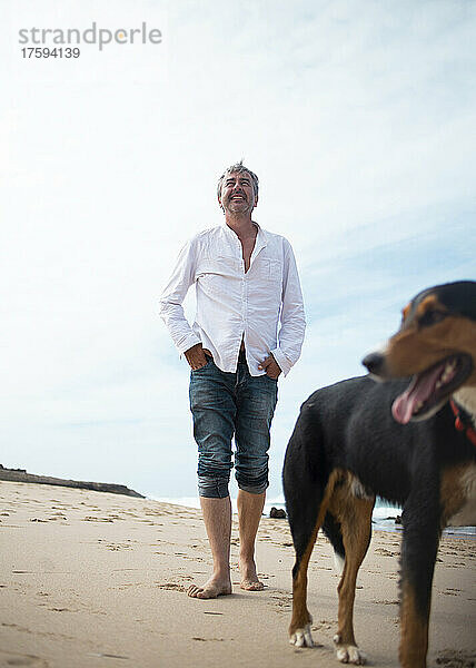 Glücklicher Mann geht mit Hund am Strand spazieren