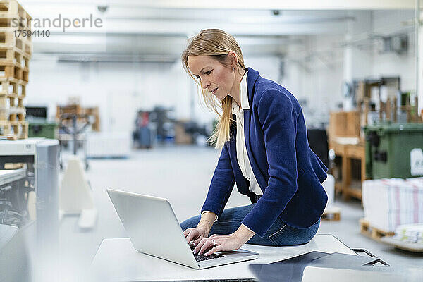 Geschäftsfrau sitzt mit Laptop am Schreibtisch in der Fabrik