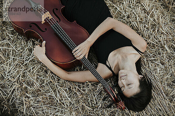 Woman with cello lying in stubble field