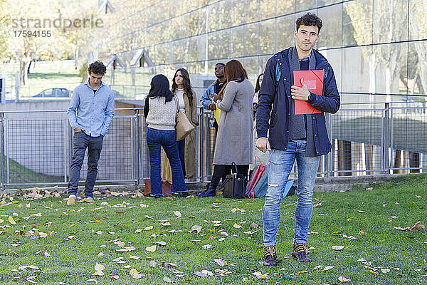 Student hält Akte mit Freunden im Hintergrund auf dem Universitätscampus