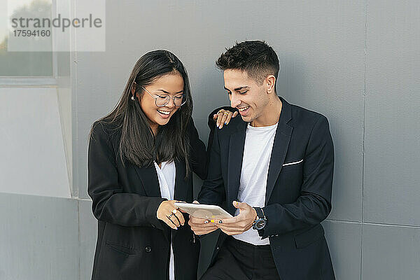 Lächelnde Geschäftskollegen teilen sich einen Tablet-PC vor einer grauen Wand