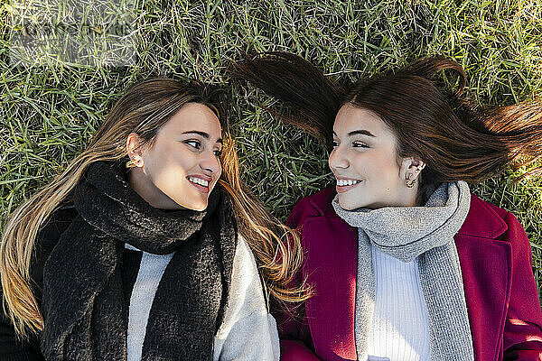 Smiling women looking at each other lying on grass