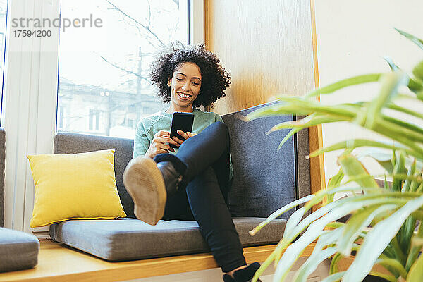 Glückliche Geschäftsfrau  die ihr Mobiltelefon auf dem Sofa benutzt