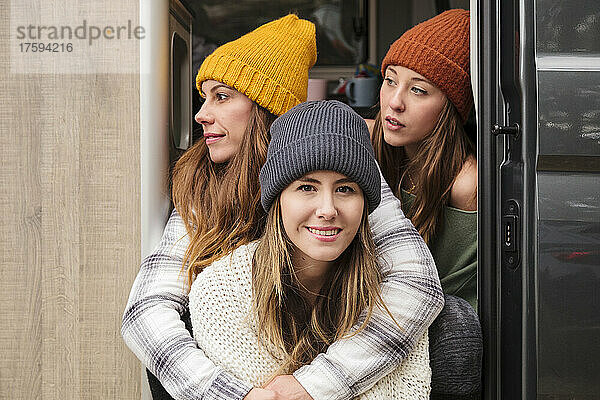 Lächelnde Freunde in warmer Kleidung sitzen an der Tür des Lieferwagens