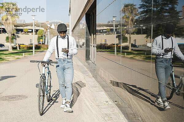 Junger Mann benutzt Smartphone und läuft mit Fahrrad auf Fußweg