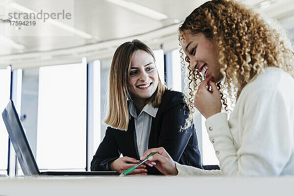 Lächelnde Geschäftskollegen mit Laptop sitzen im Coworking-Büro