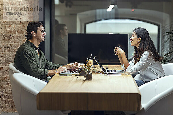 Geschäftsmann und Geschäftsfrau mit Laptops diskutieren am Schreibtisch im Coworking-Büro