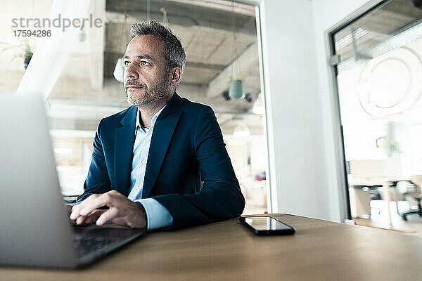 Dedicated businessman using laptop sitting at desk in office