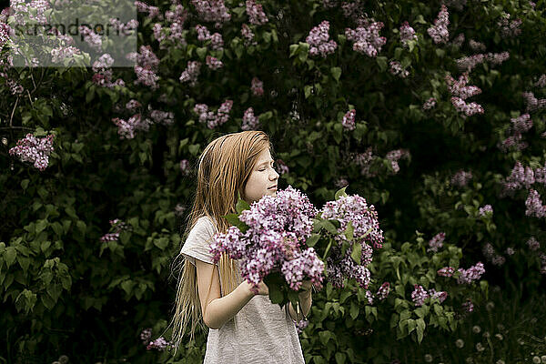 Blondes Mädchen mit geschlossenen Augen hält lila Blumen in der Natur