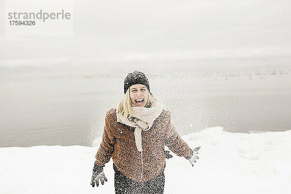 Sorglose Frau in warmer Kleidung spielt im Winter mit Schnee