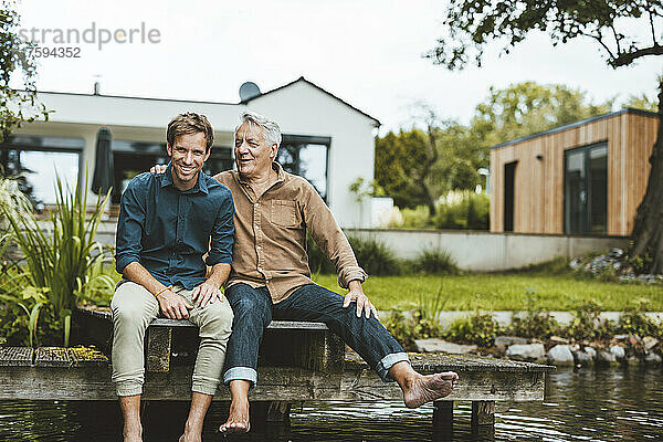 Glücklicher Vater und Sohn sitzen auf dem Steg am See im Hinterhof