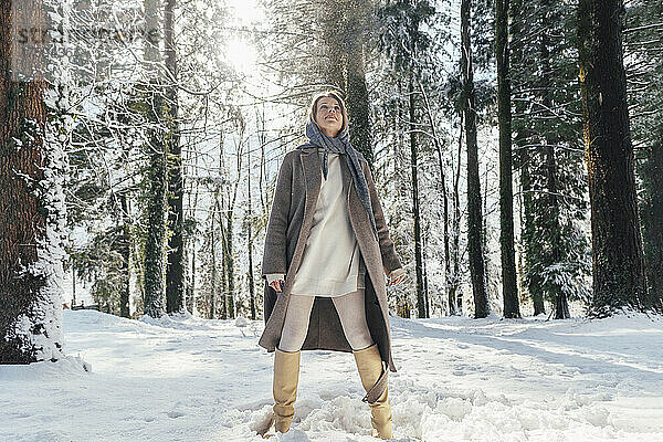 Frau in warmer Kleidung steht im tiefen Schnee im Wald
