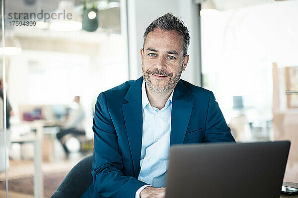 Smiling businessman sitting with laptop at workplace