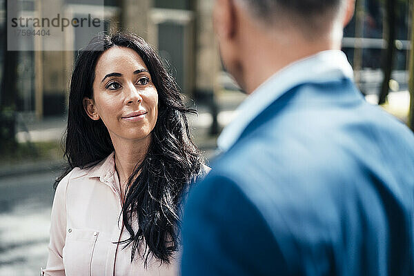 Lächelnde Geschäftsfrau blickt Geschäftsmann am Fußweg an