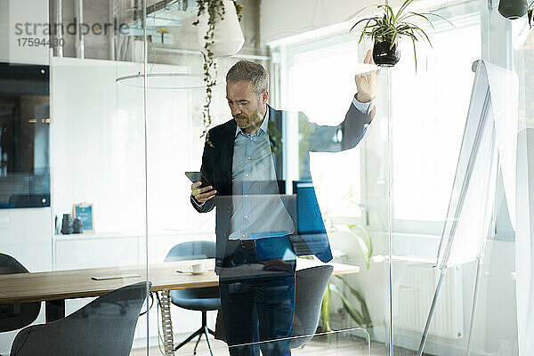 Businessman using tablet computer in meeting room seen through glass wall