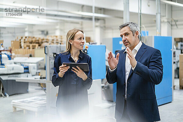 Blonde Geschäftsfrau mit Tablet-PC schaut Kollegen beim Diskutieren in der Fabrik zu