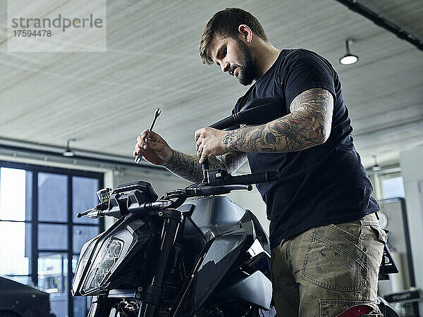 Tätowierter Mechaniker mit Werkzeug arbeitet in der Werkstatt am Motorrad