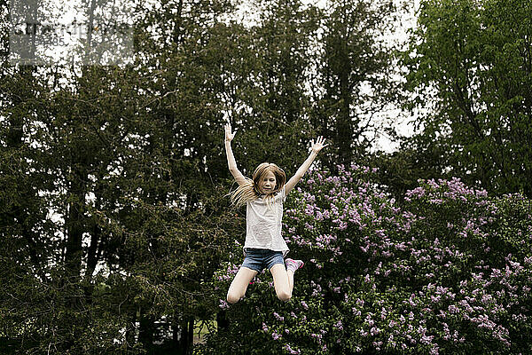 Fröhliches Mädchen springt vor lila Blumen in der Natur
