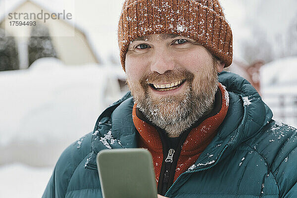 Glücklicher Mann mit Handy im Winter