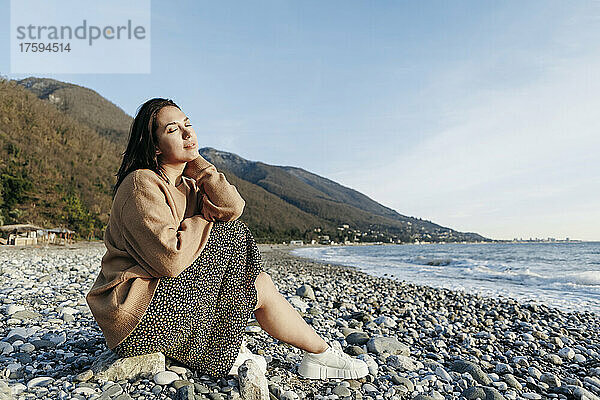 Schöne junge Frau sitzt auf Steinen am Strand