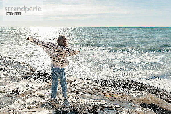 Teenage girl with arms outstretched looking at sea standing on rock at beach