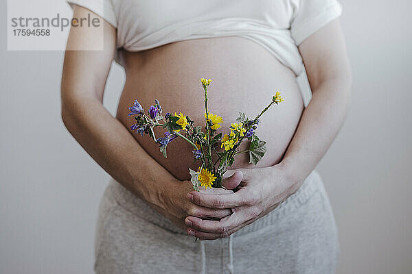 Schwangere Frau mit Blume vor der Wand zu Hause