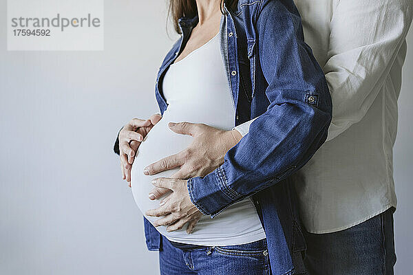 Mann umarmt schwangere Frau an der Wand