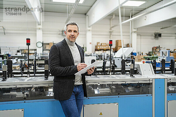 Geschäftsmann mit Tablet-PC steht neben Maschinen in der Fabrik