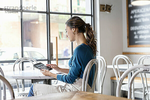 Unternehmer benutzt Taschenrechner auf Tisch im Café