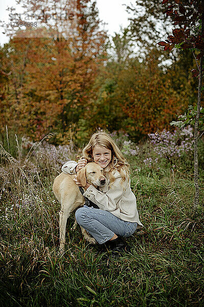 Lächelndes blondes Mädchen umarmt Hund im Garten