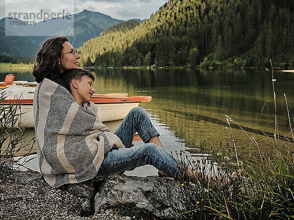 Mutter und Sohn sitzen in eine Decke gehüllt am Seeufer