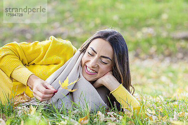 Glückliche junge Frau mit Blatt  das im Herbstpark auf Gras liegt