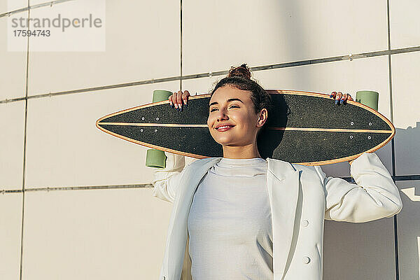 Nachdenkliche junge Frau mit Skateboard vor der Wand