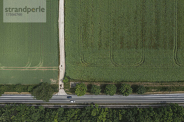 Drohnenansicht einer Landstraße  die sich am Rande eines grünen Feldes erstreckt