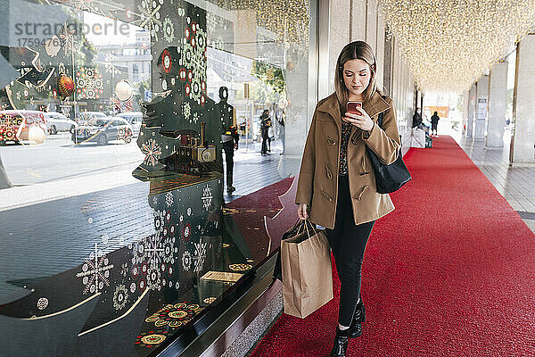 Frau mit Einkaufstüten benutzt Smartphone auf Fußweg