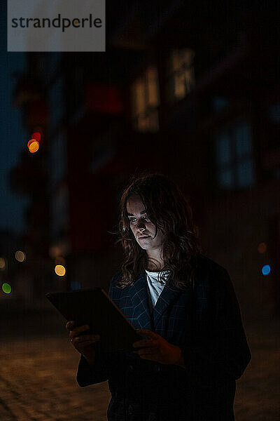 Junge Frau benutzt nachts Tablet-PC auf der Stadtstraße