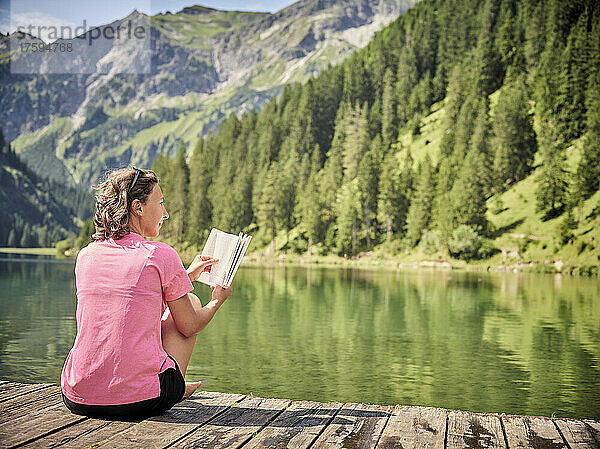 Frau mit Buch träumt Tag auf Steg am See