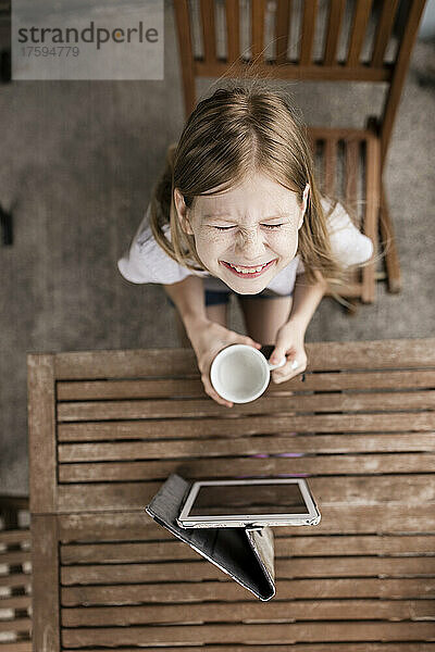 Lächelndes Mädchen mit Milchbecher und Tablet-PC auf dem Tisch