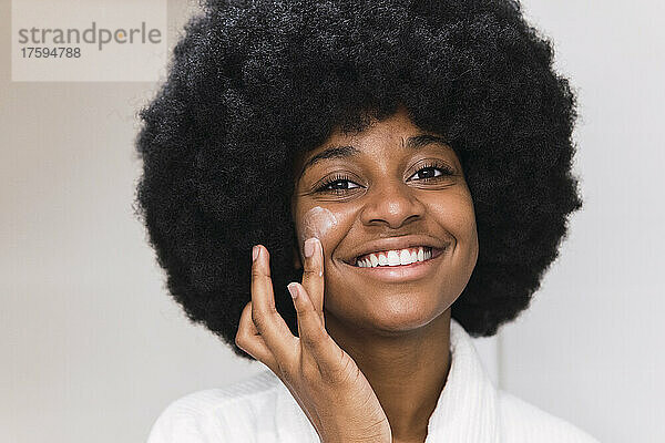 Lächelnde Afro-Frau  die Gesichtscreme aufträgt