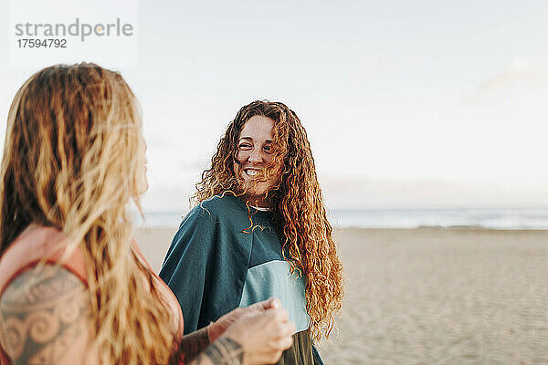 Lächelnde Frau im Gespräch mit einer Freundin am Strand