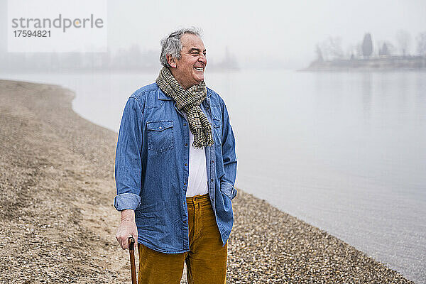 Lächelnder Mann mit Schal steht am Strand