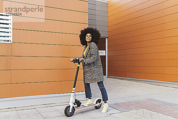 Frau mit Elektroroller steht auf Fußweg